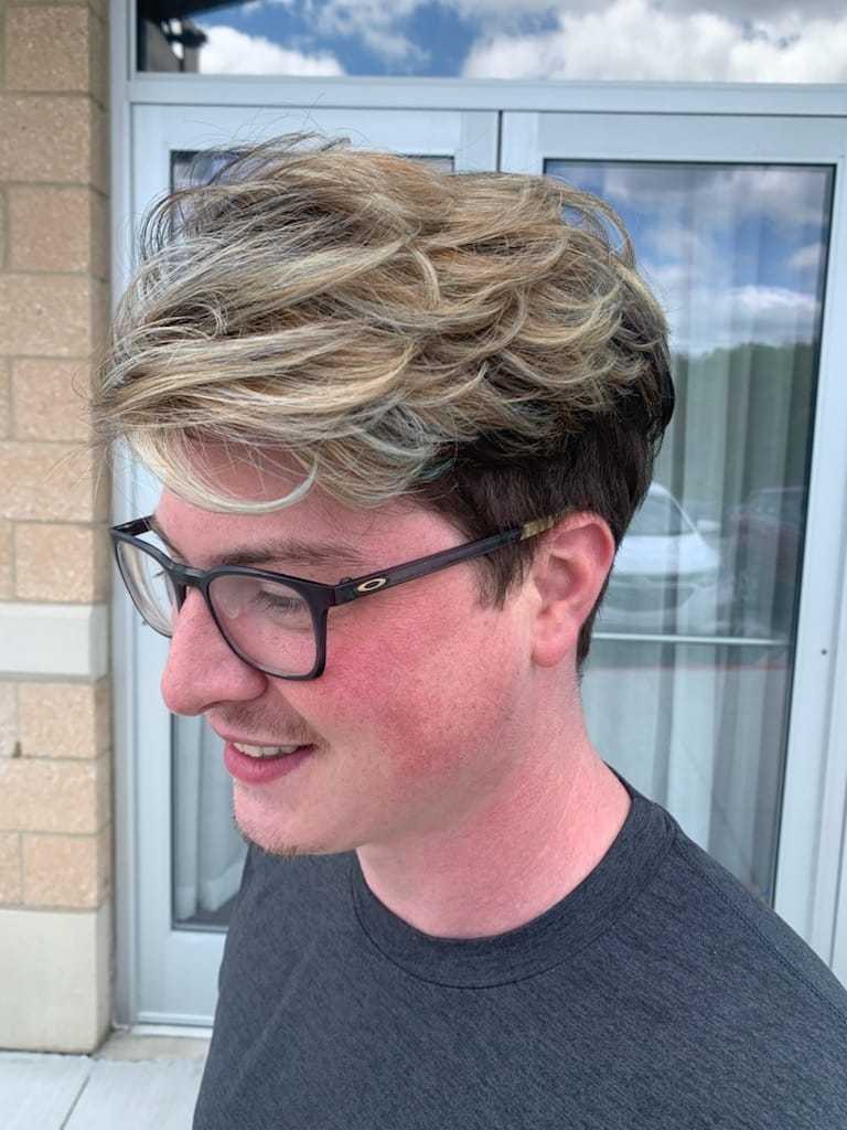Man with stylish blonde highlights and glasses outside a building.