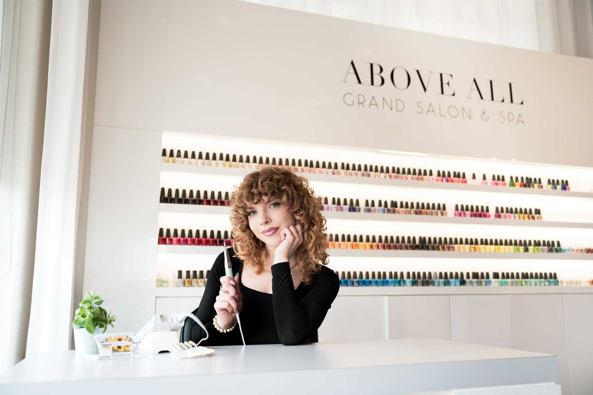 Woman at nail salon reception desk, surrounded by colorful nail polishes.