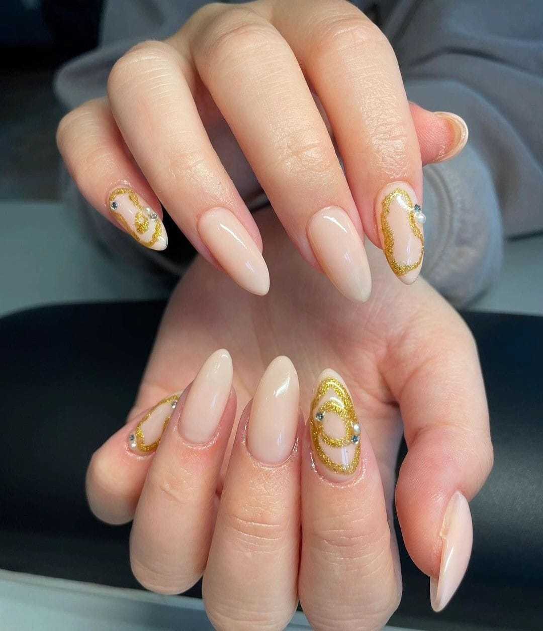 Elegant nails with gold and white abstract designs on almond-shaped tips.