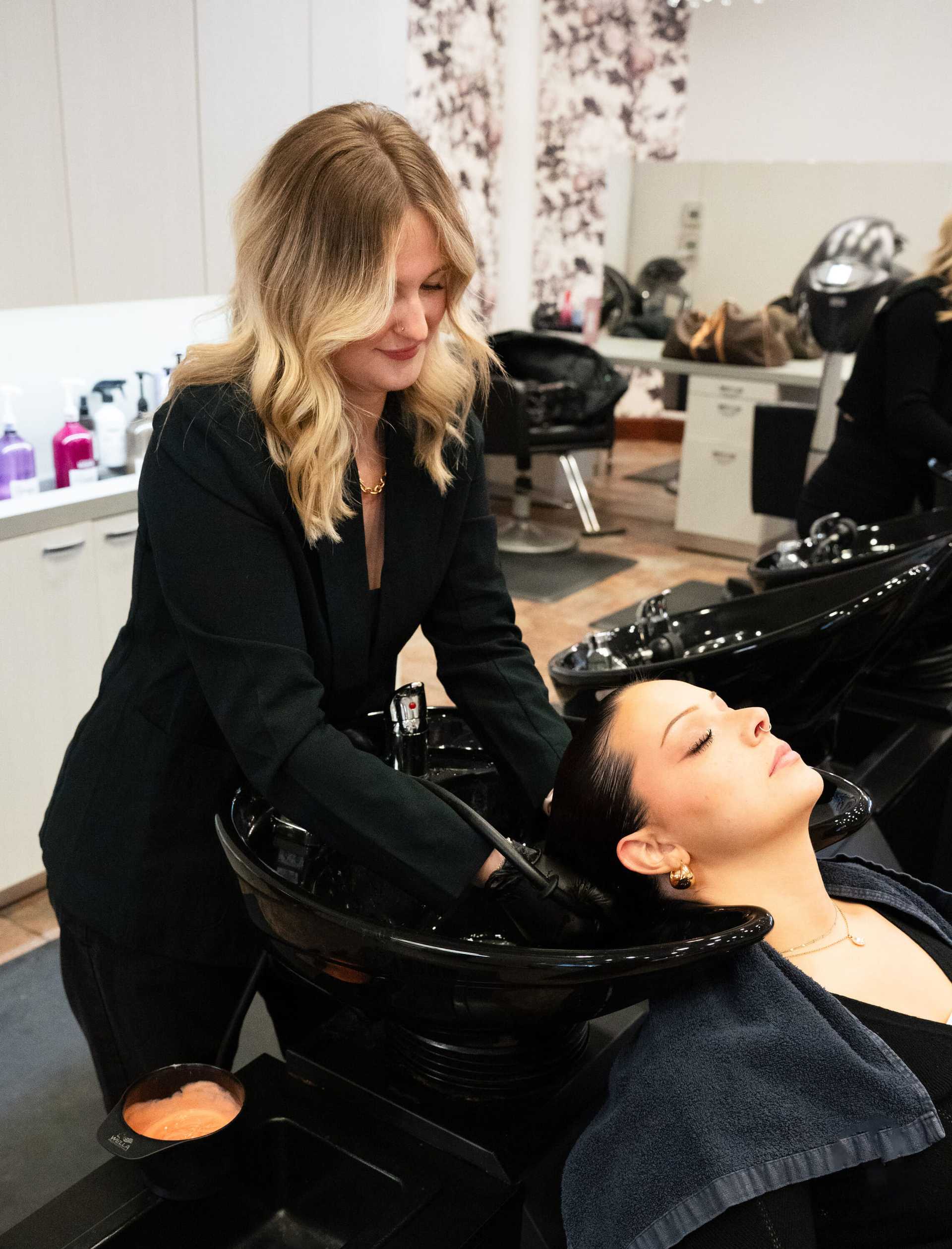 Hairdresser washing client's hair at salon sink.