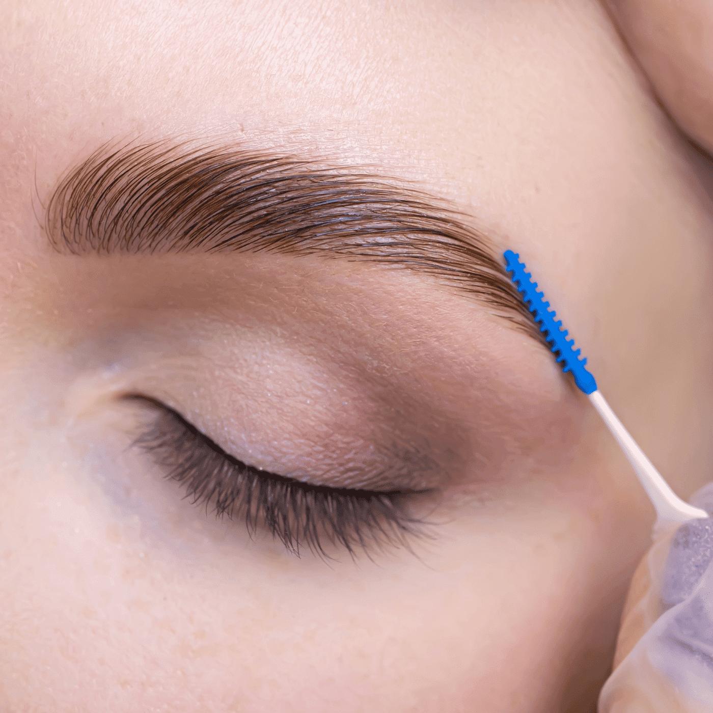 Eyebrow being brushed with a blue tool, showing beauty care routine close-up.