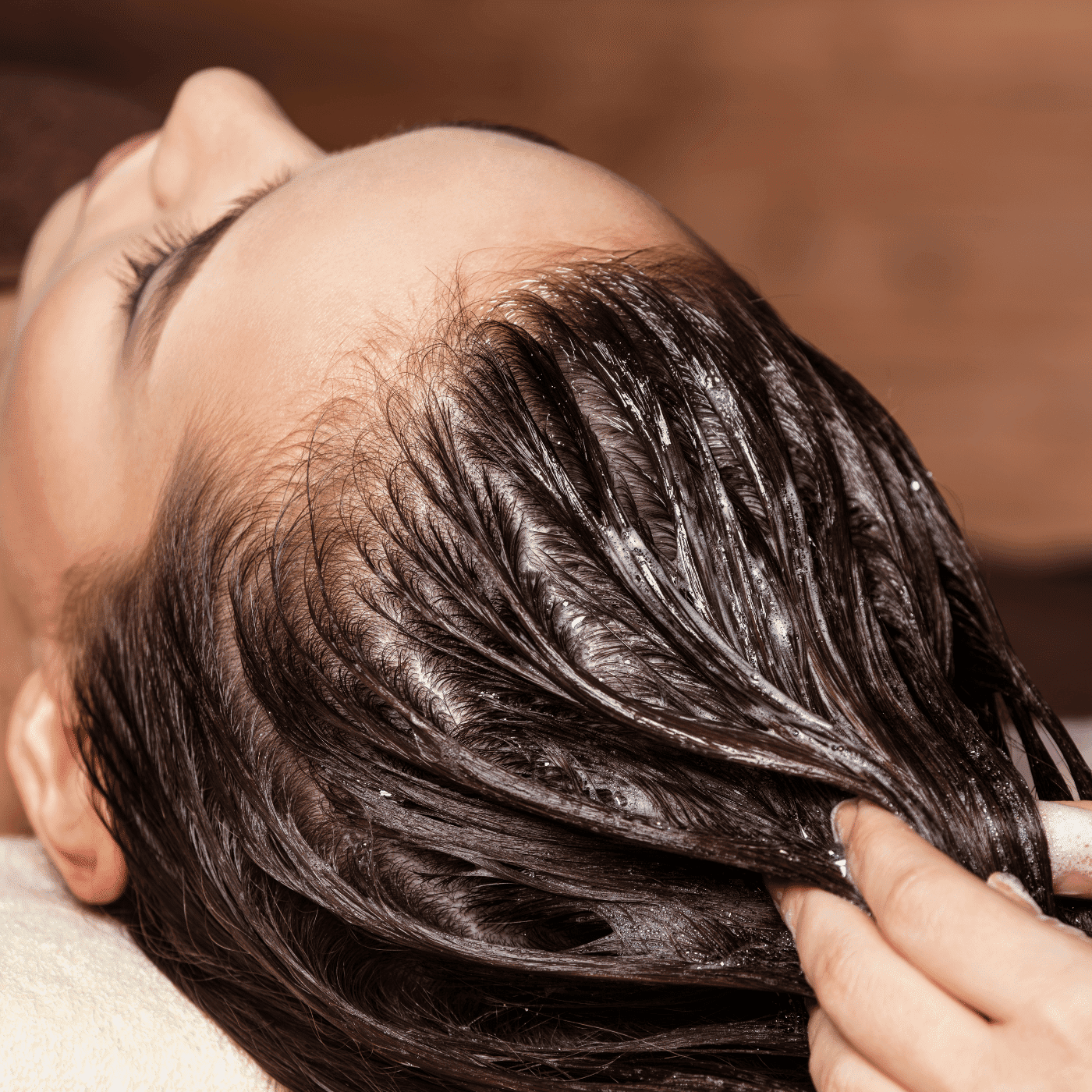 Applying a nourishing hair treatment to a woman's scalp and hair in a salon setting.