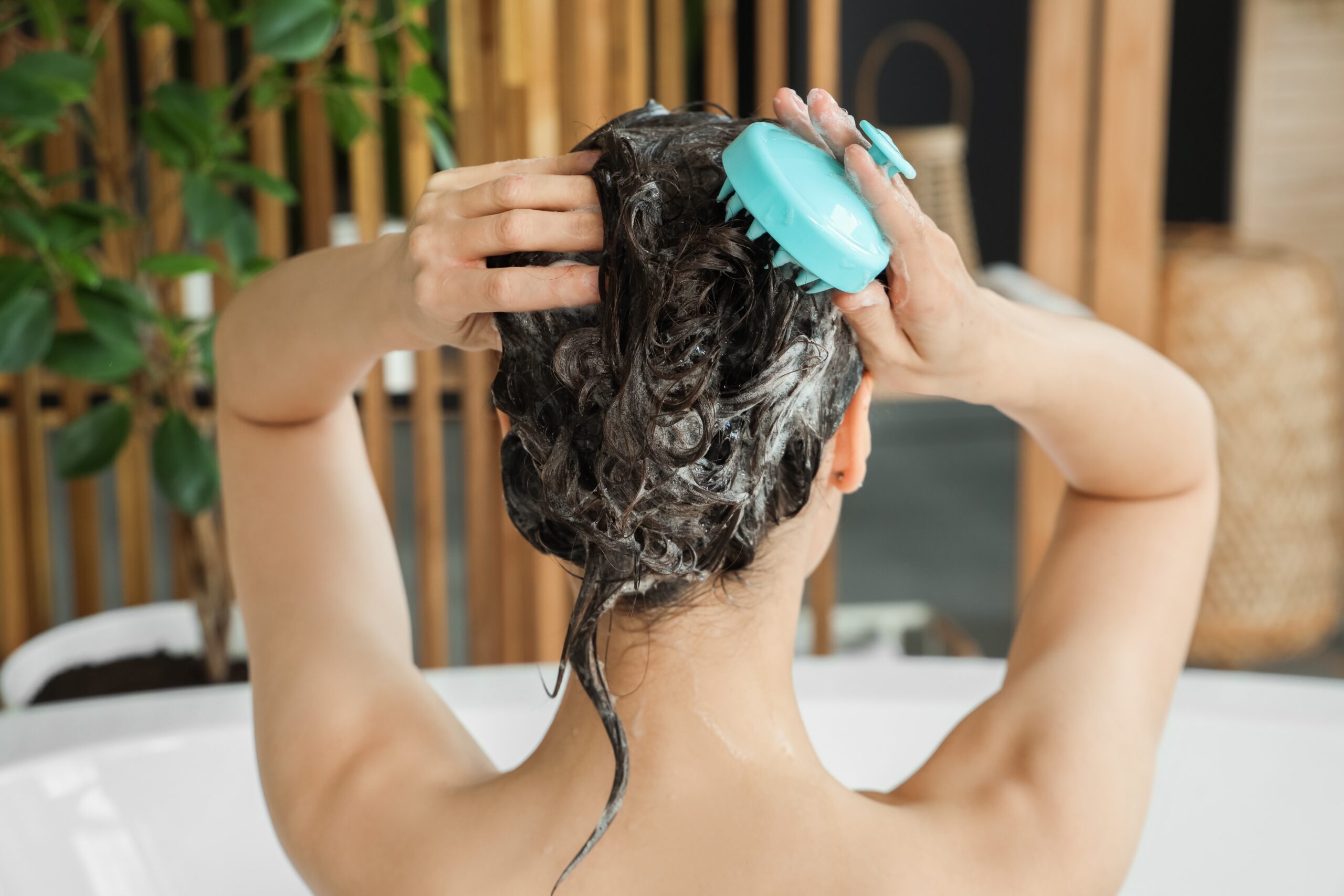 How Often Should You Really Wash Your Hair? at Above All Grand Salon & Spa — stylist washing hair in salon sink for a healthy scalp and shiny strands.